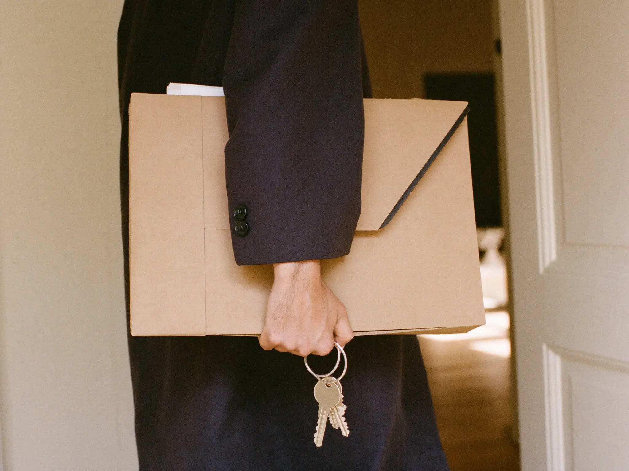Una persona con abrigo lleva una carpeta con forma de sobre bajo el brazo y las llaves en la mano, lista para salir