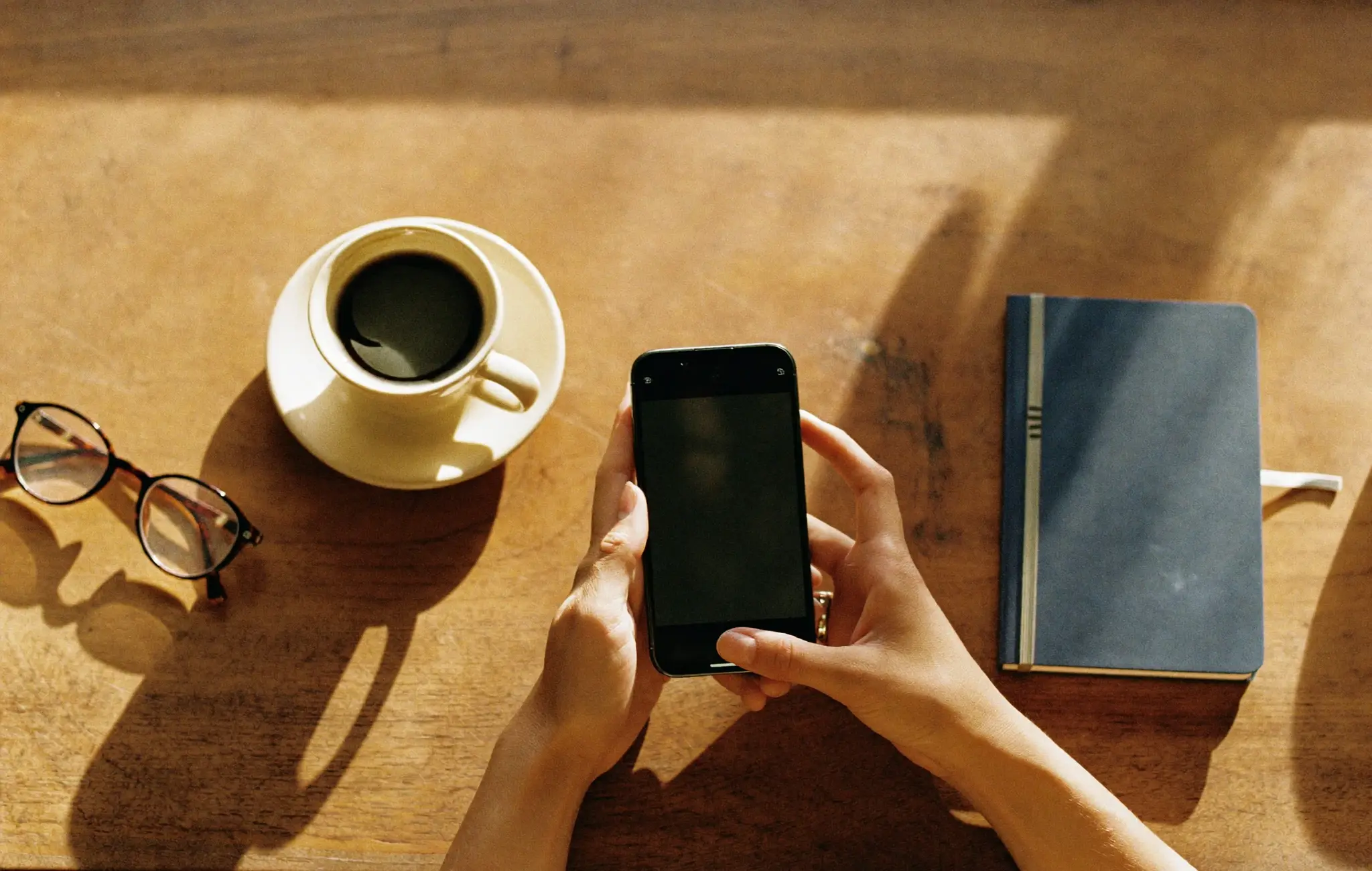 Unas manos sostienen un móvil sobre la mesa de la cocina, junto a un café